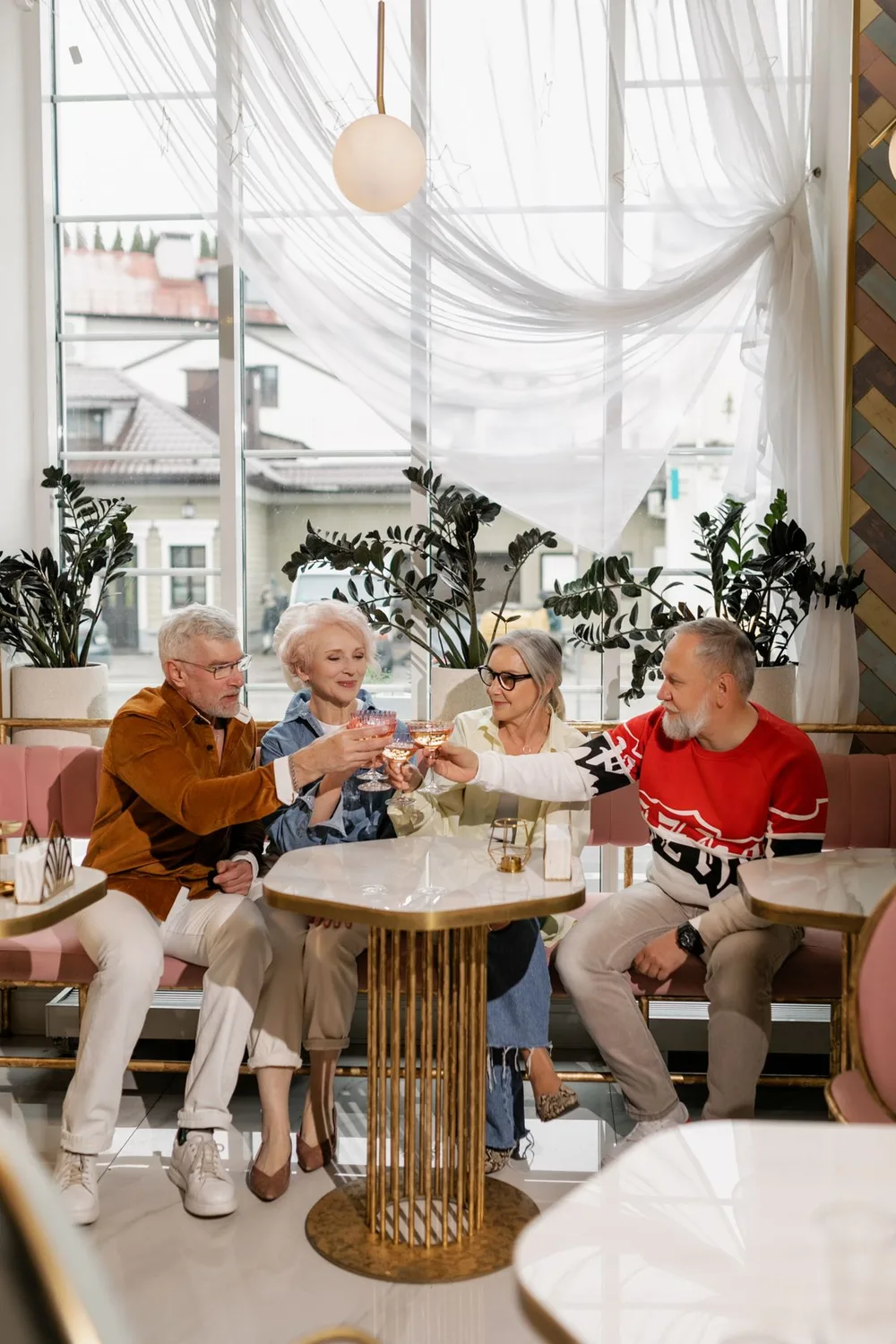 Four older friends seated around a cafe table raising glasses together